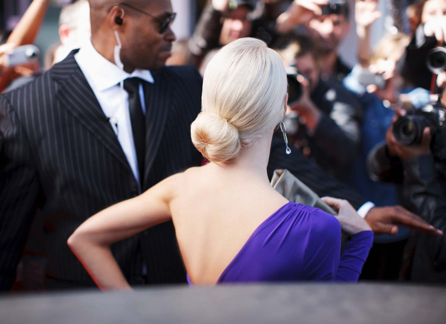A celebrity in a purple dress at a red carpet event with a personal bodyguard.
