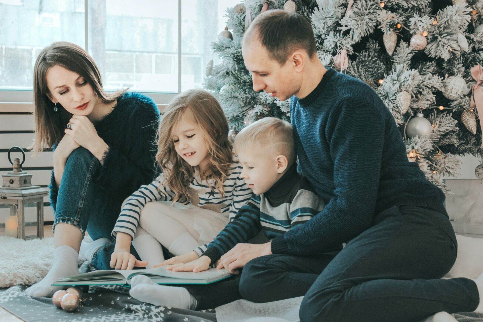 A family with two young children enjoying a Christmas storybook together in a cozy, festively decorated room.