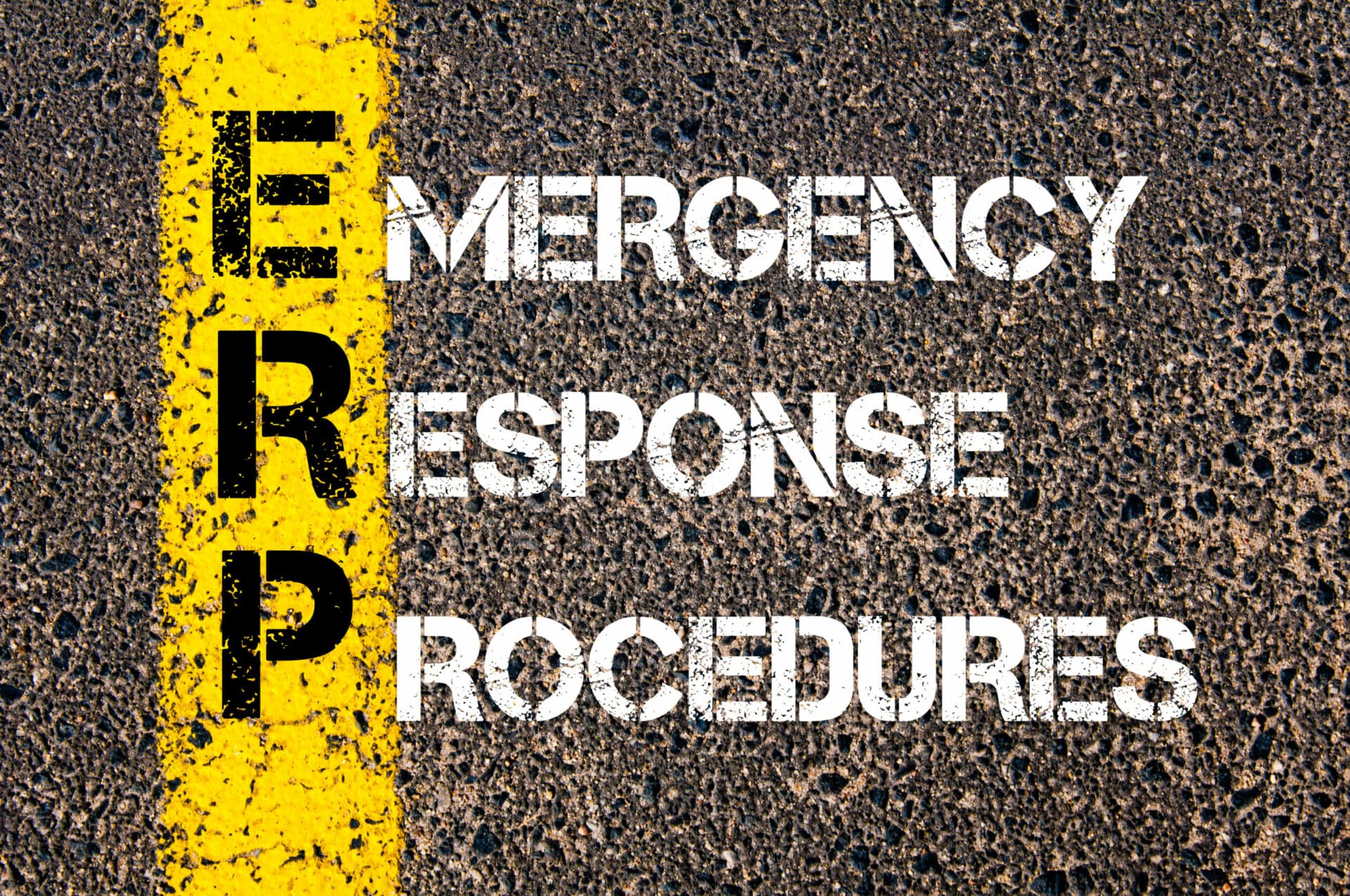 Text 'Emergency Response Procedures' painted in white over a yellow line on a textured asphalt surface, indicating safety protocols