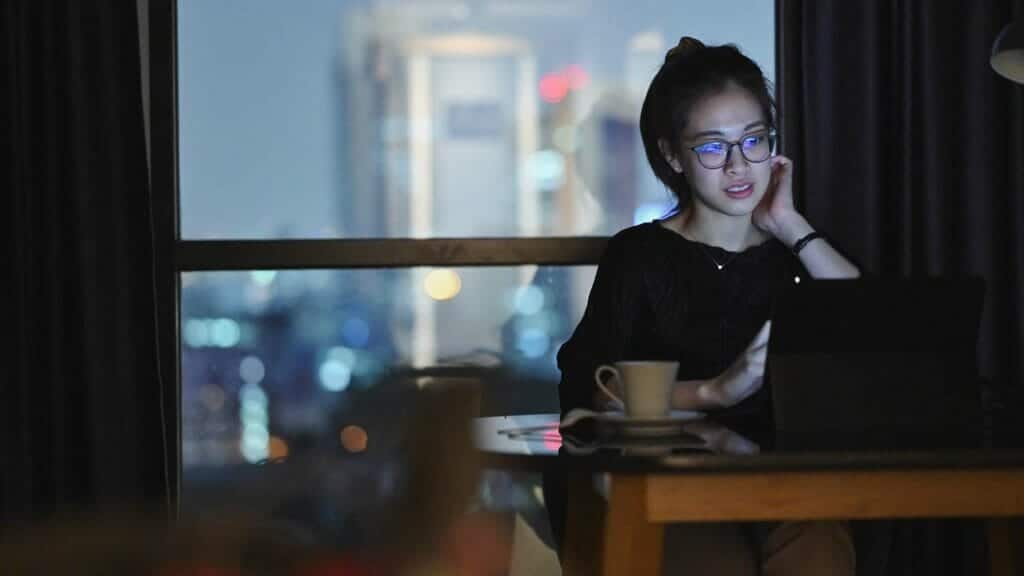 Young woman working on a laptop at night with the city lights in the background, reflecting deep concentration and late-hour productivity.