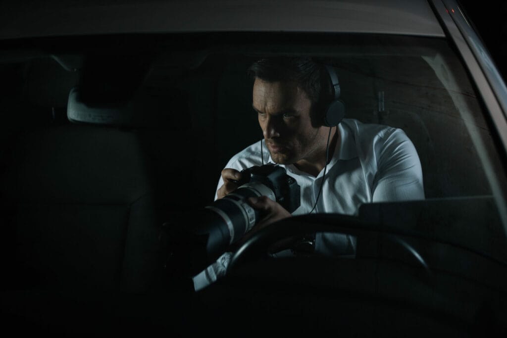 Man in a white shirt and headset using a camera with a telephoto lens inside a car at night