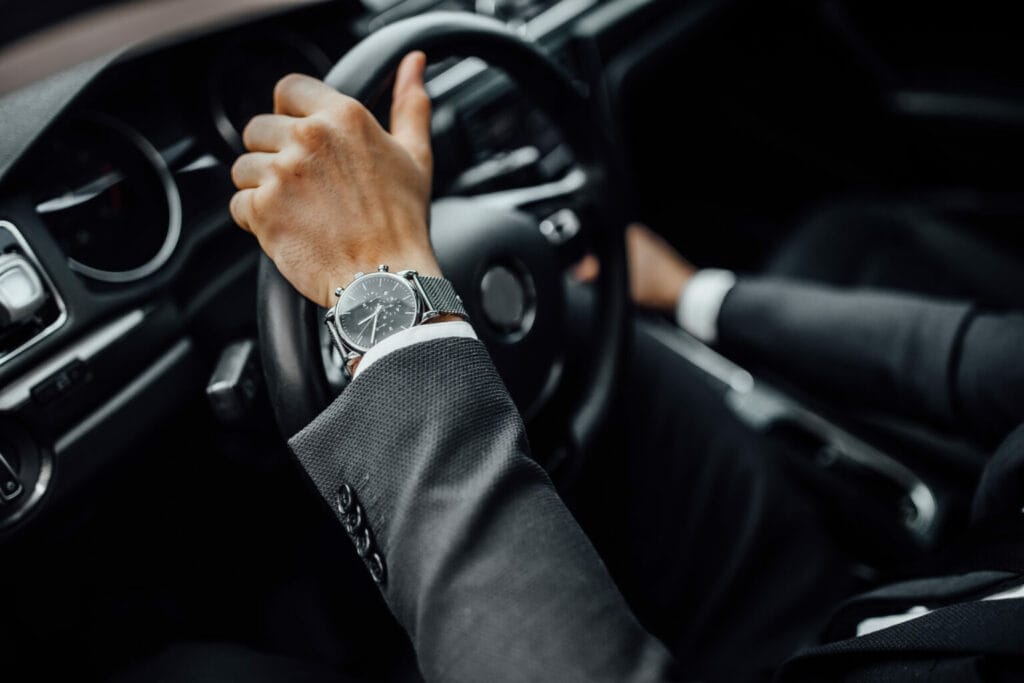 Close-up of hands with a wristwatch on a car's steering wheel.