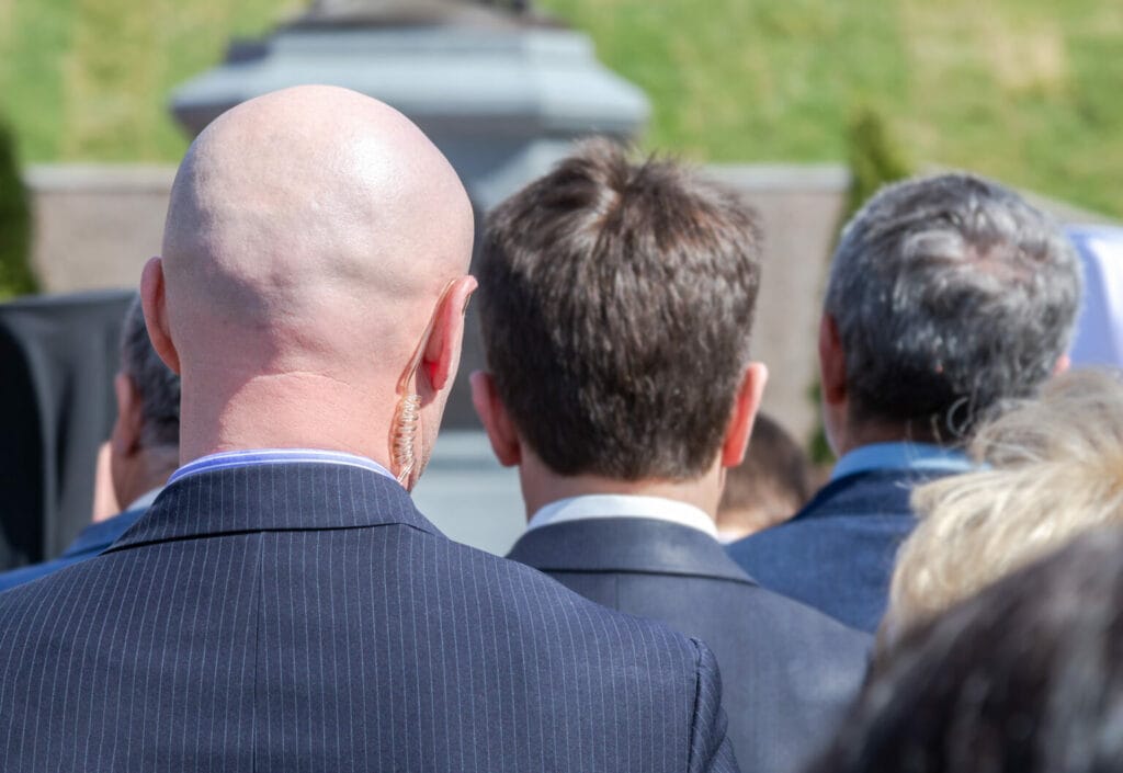 Back view of a bald security professional with an earpiece focused ahead.