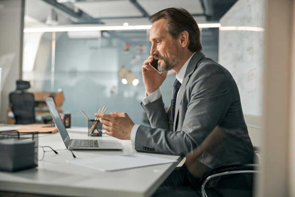 Mature businessman concentrating on a phone call while working at his desk in a modern office.