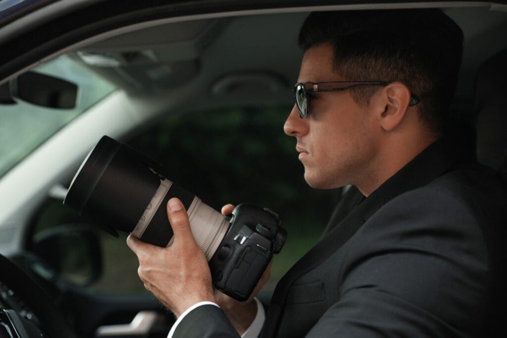 Man in sunglasses and a suit holding a professional camera inside a vehicle