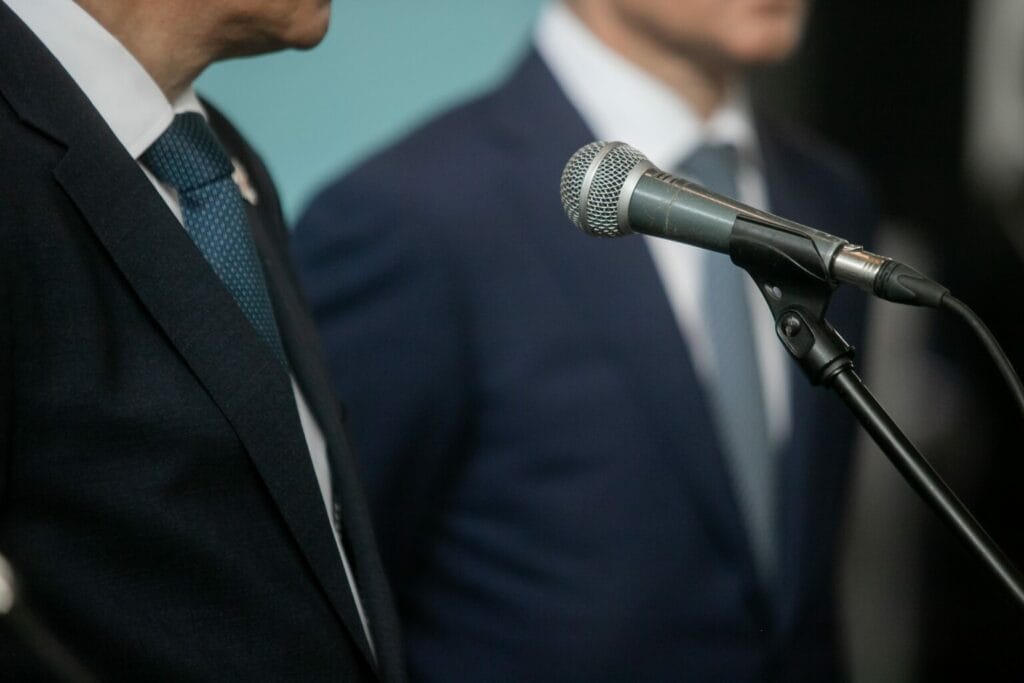 Microphone in focus with a male speaker in the background wearing a business suit.