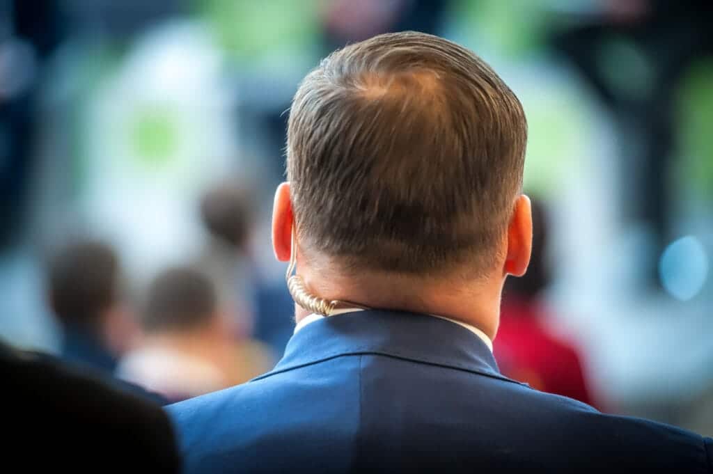 Back view of a security agent with an earpiece, overseeing a crowded event.