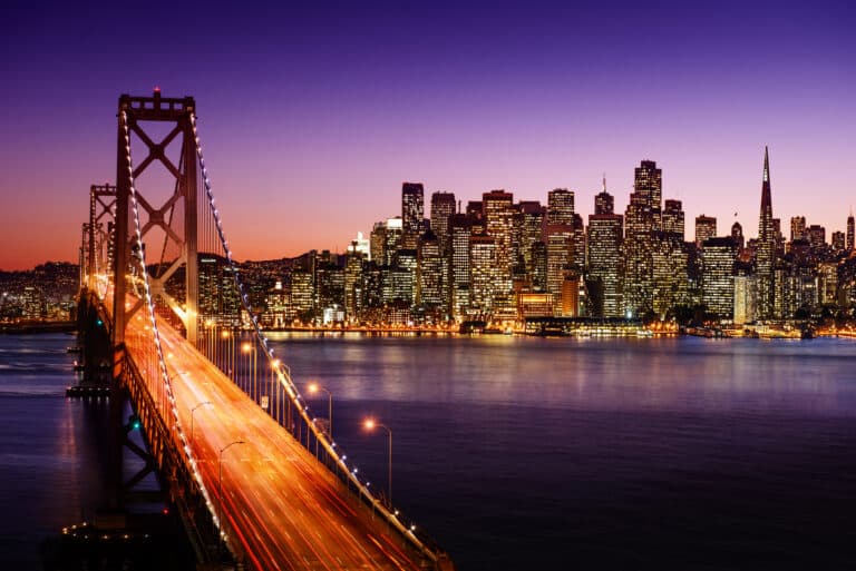 San Francisco Bay Bridge leading into the cityscape lit up at twilight.