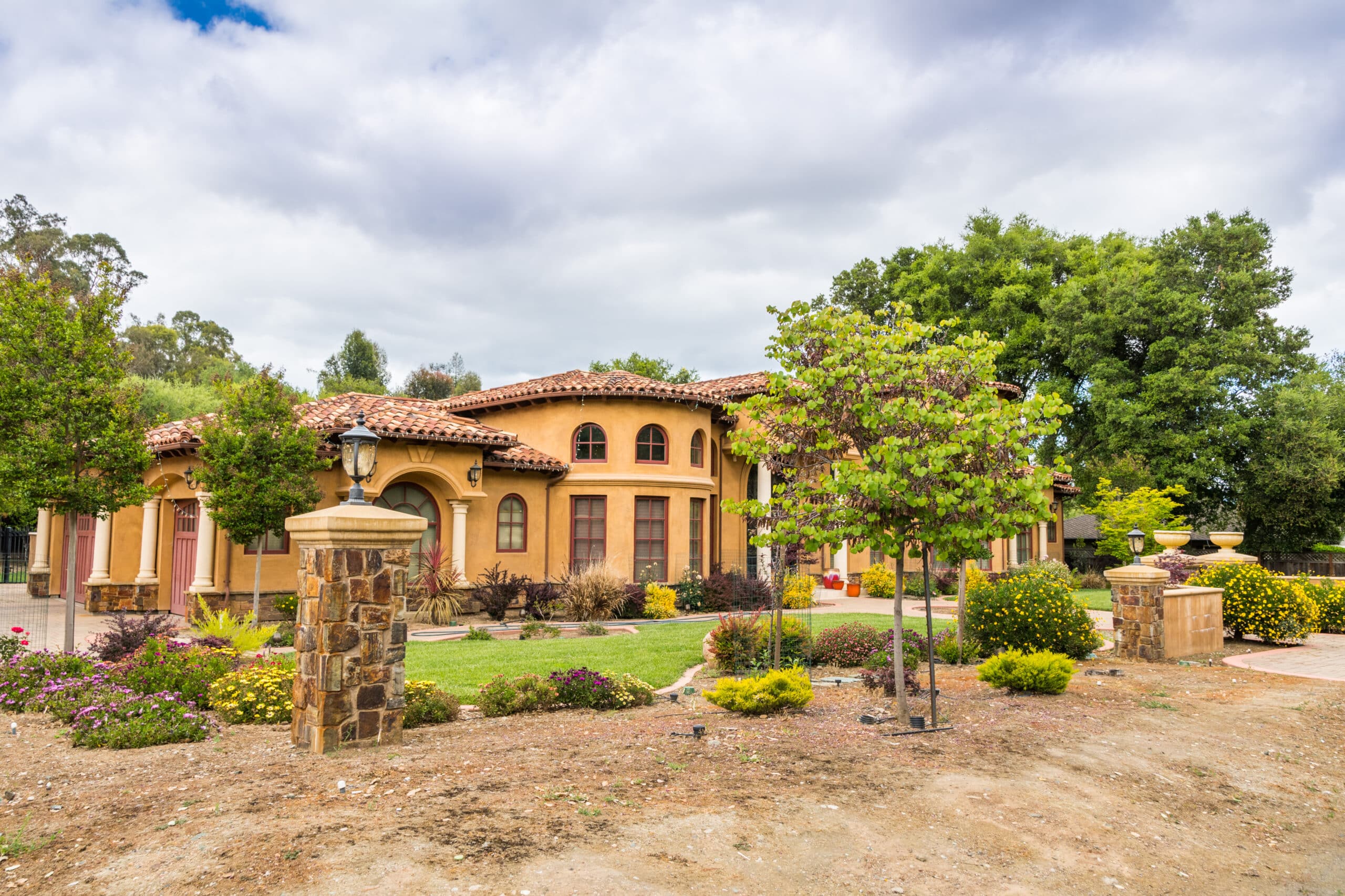 Luxurious Mediterranean-style villa with landscaped gardens under a cloudy sky in Saratoga