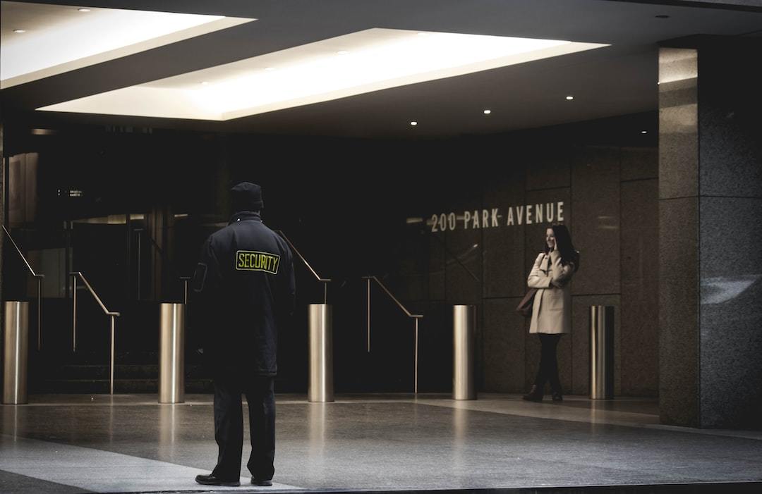 Security guard in uniform standing vigilantly in front of the 200 Park Avenue building entrance with a woman in the background.