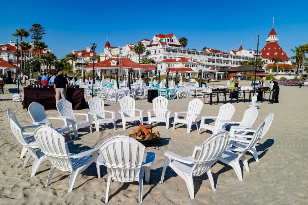A private event set up on Coronado Beach with rows of white chairs and a fire pit, Hotel del Coronado in the background.