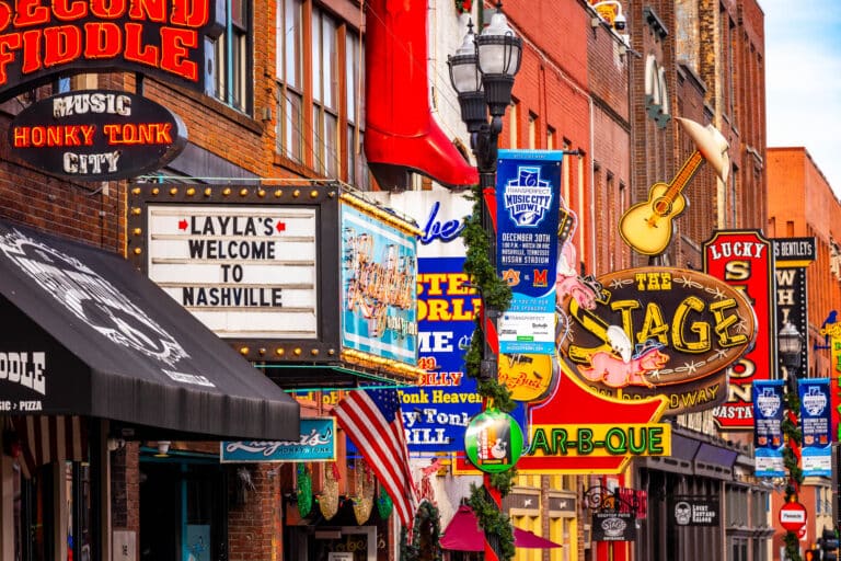 Colorful street view of Nashville's famous music and nightlife strip with neon signs and banners.