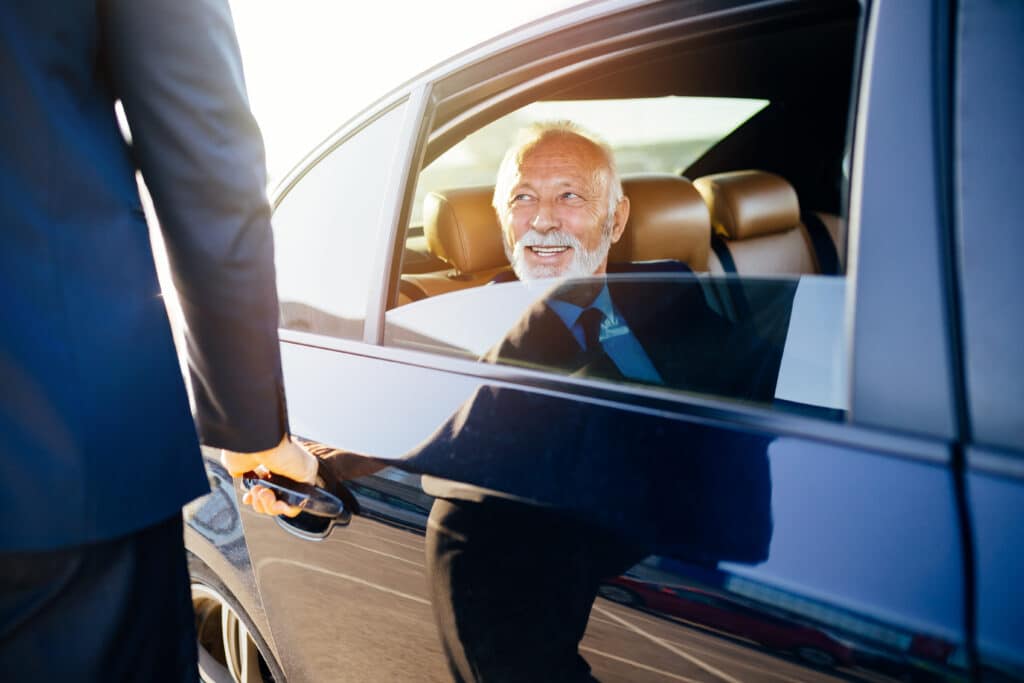 A distinguished elderly gentleman smiling warmly in the backseat of a luxury car, demonstrating the client satisfaction and security provided by Global Risk Solutions, Inc.