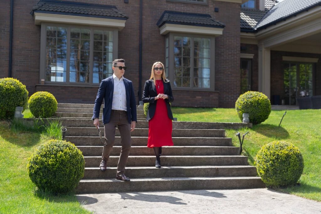 The Psychology Of Protection: Understanding The Client’s Needs And Managing Their Expectations 4 A male security professional accompanies a female client outside a luxurious home, addressing client needs in security with personalized protection services.