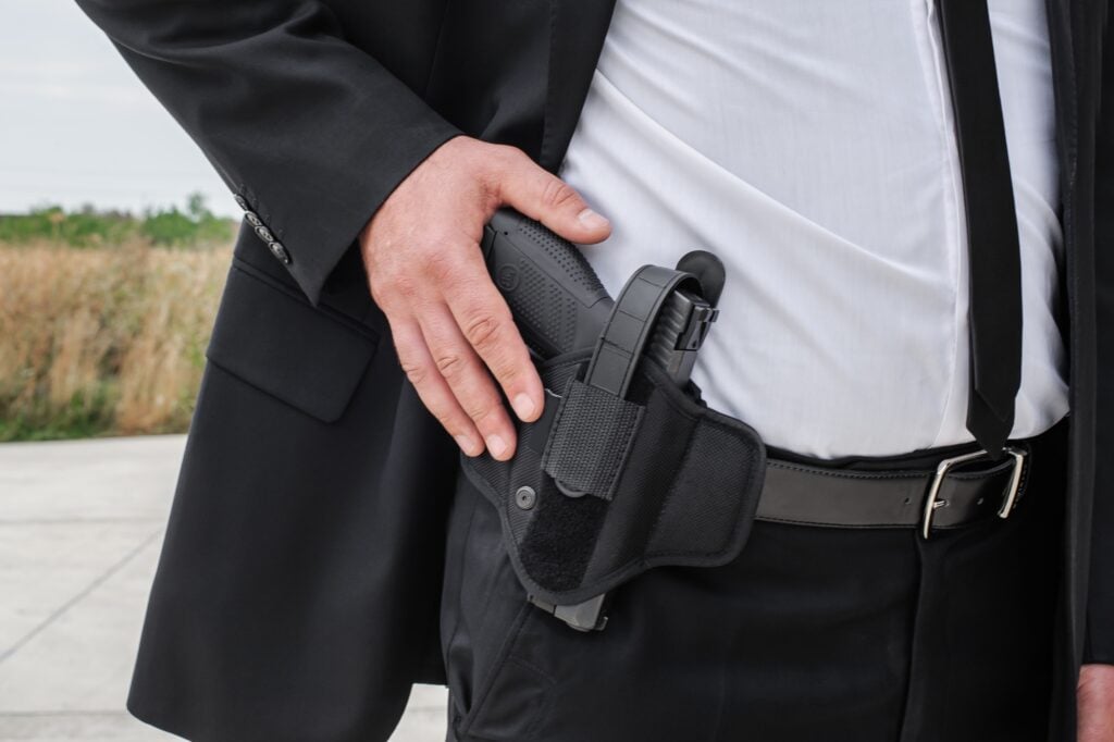Essential Gear For Close Protection Agents: What The Pros Rely On 3 Close-up of a security professional’s hand resting on a holstered firearm, showcasing essential gear for protection services.