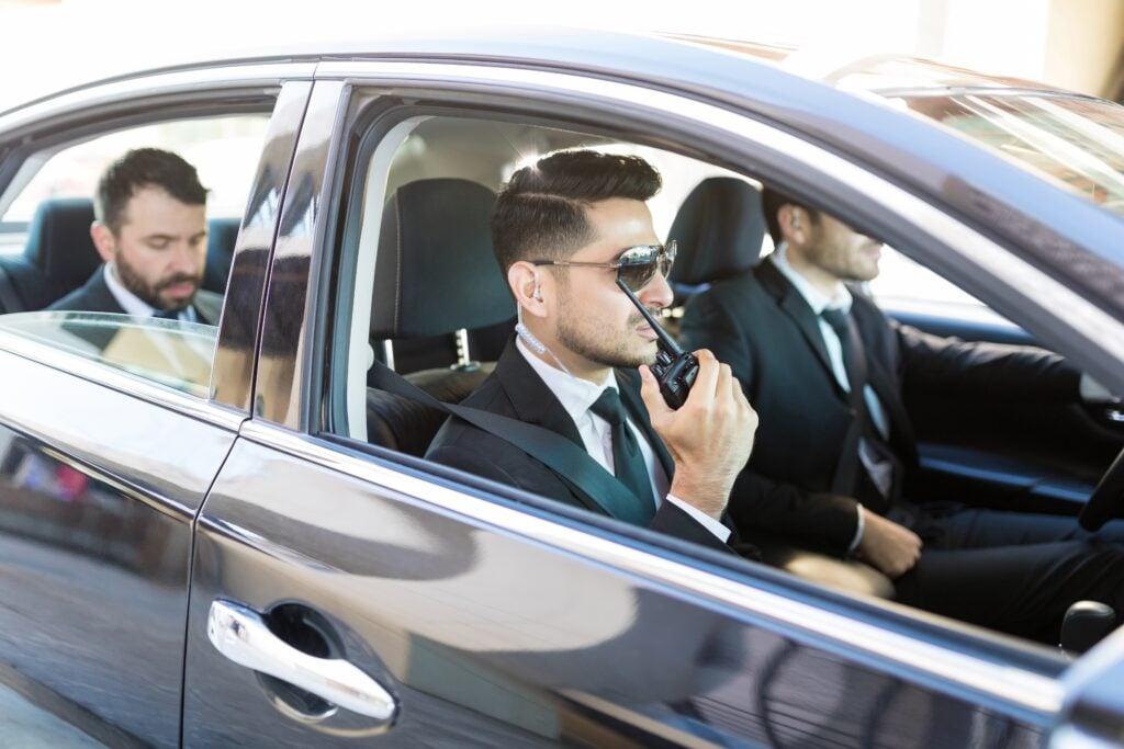 The Future Of Close Protection Services: Trends, Innovations, And Predictions 5 Close protection team inside a vehicle, with a bodyguard using a radio transceiver to ensure seamless communication, symbolizing the future of close protection services with advanced mobility and teamwork.