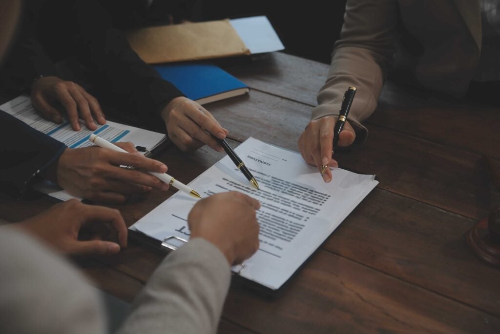 Close-up of business professionals reviewing legal documents at a wooden table, addressing Legal and Ethical Challenges through teamwork and collaboration.