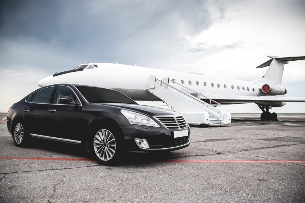 Luxury black sedan parked near a private jet on the tarmac, symbolizing executive airport transportation and security.
