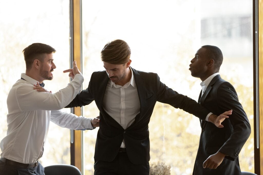 Two colleagues holding back an angry man during a workplace altercation in a modern office setting.