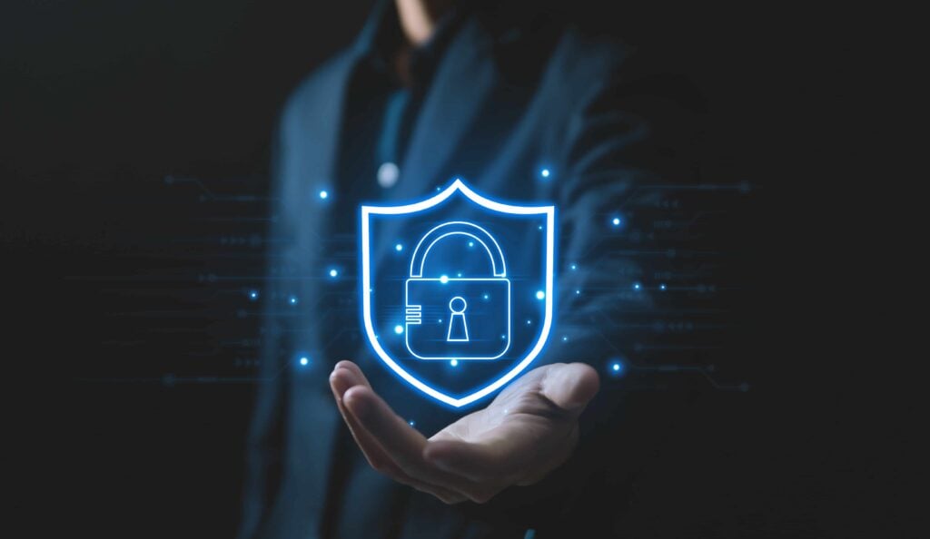 A businessman’s hand holding a glowing shield icon with a lock, symbolizing leveraging technology to ensure safety and protection.