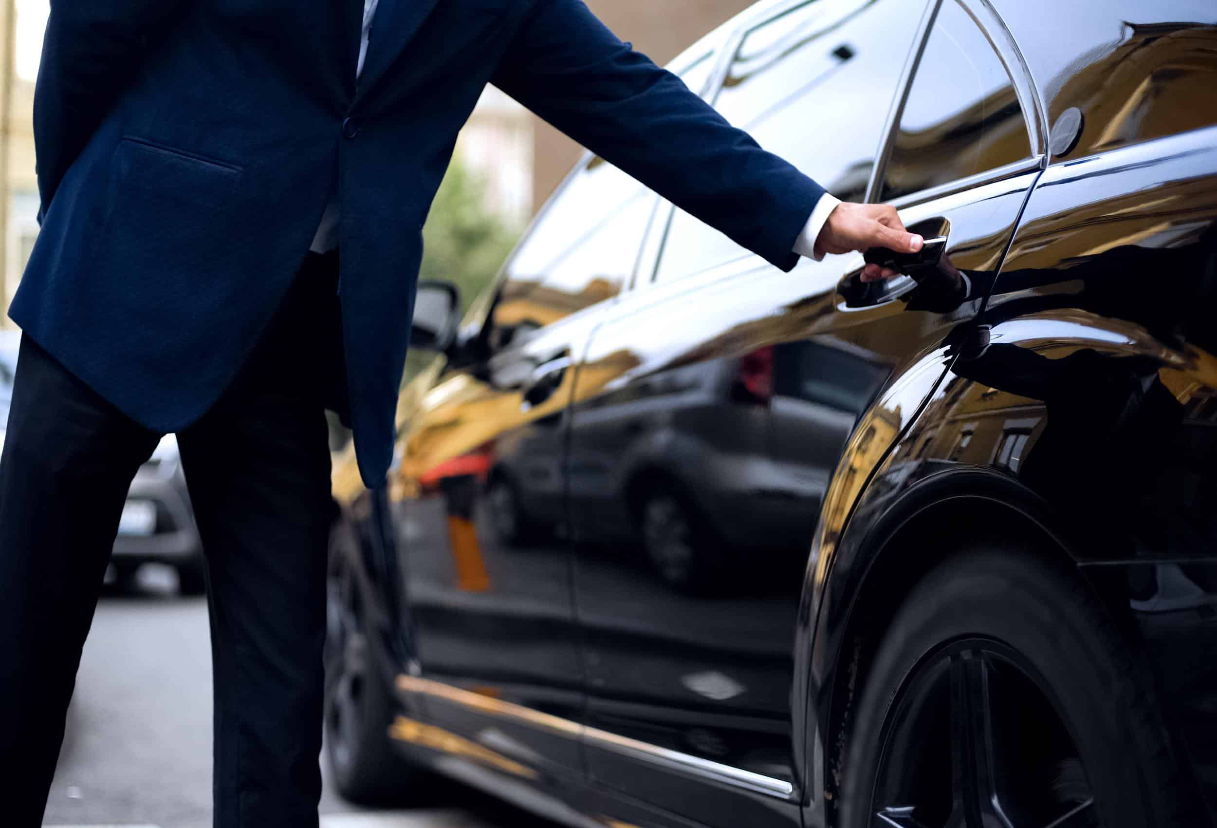 Security driver in navy suit opening the door of a luxury black vehicle for Armed Security Transport