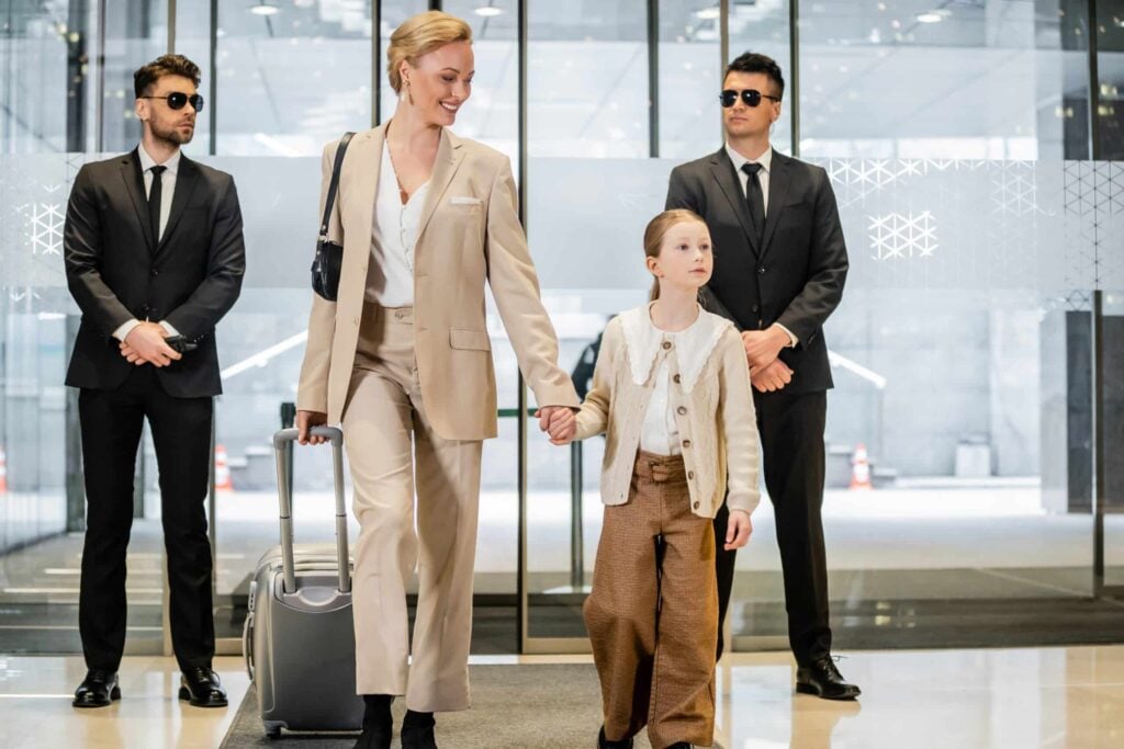 What Security Professionals Wear: Bodyguards in formal suits escorting a woman and child through a corporate lobby.