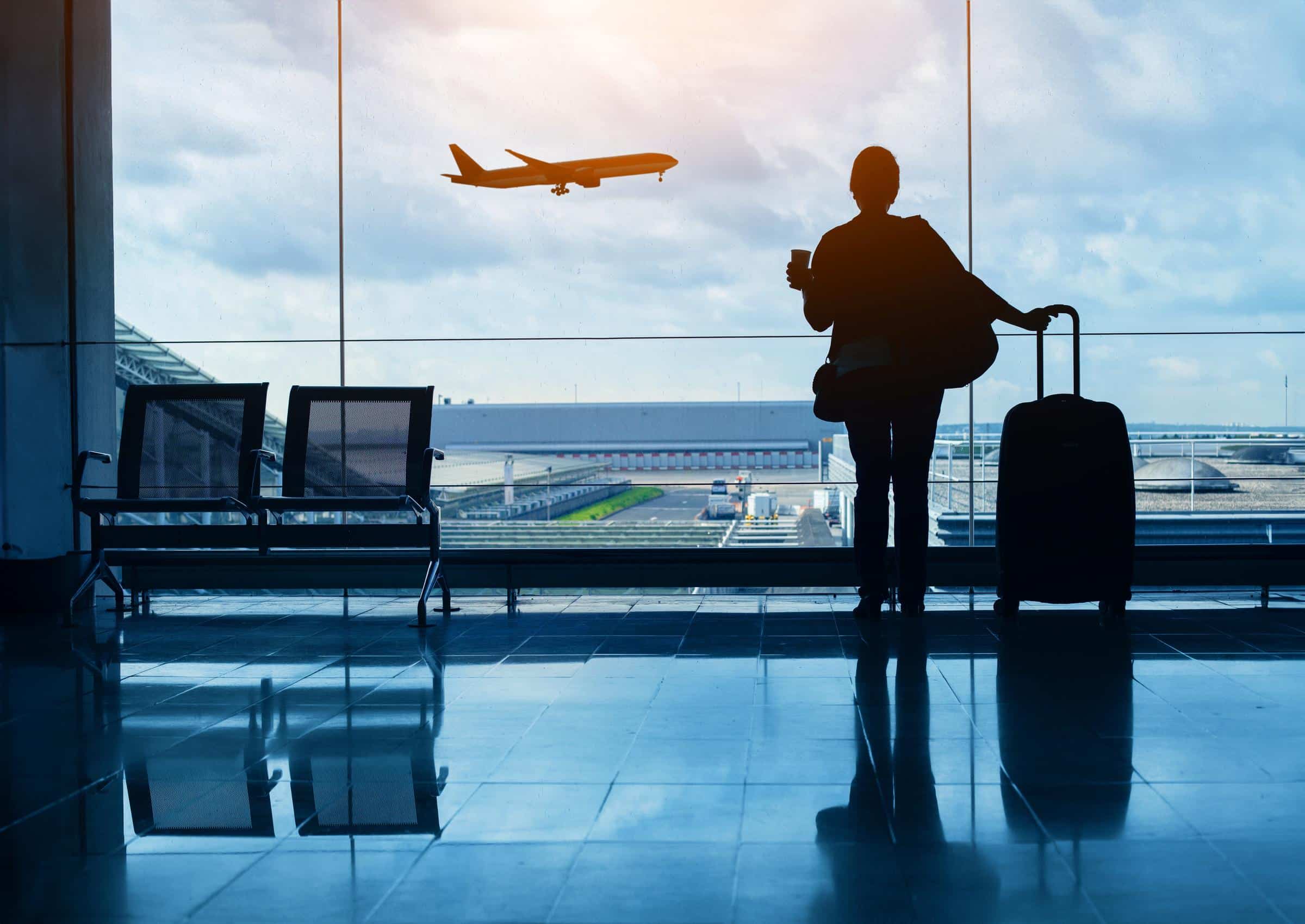 Traveler standing at an airport window watching a plane take off representing International Travel Security Tips and the importance of safe global travel preparation.