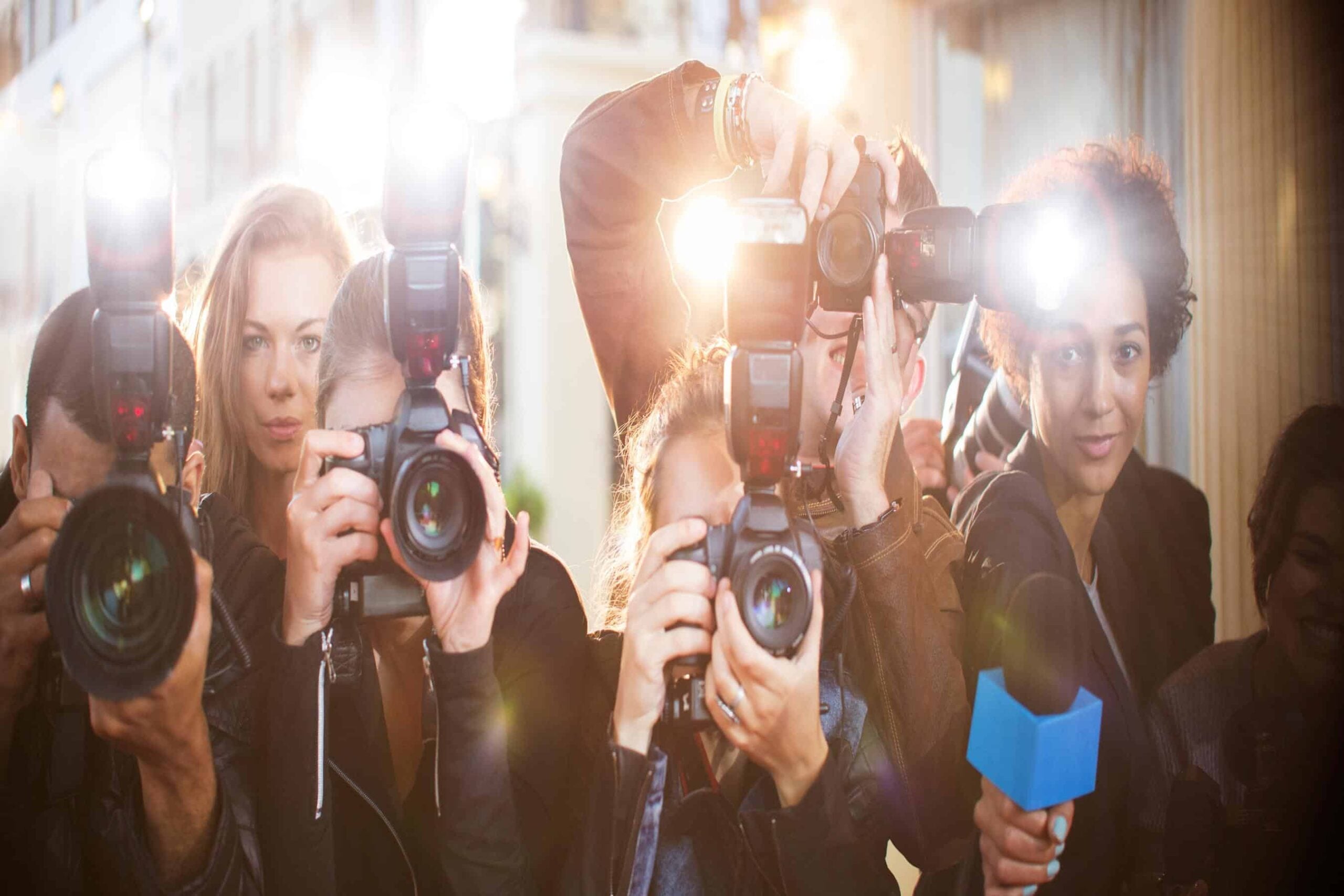 A group of paparazzi photographers pointing cameras and flashing lights, illustrating the need for paparazzi management strategies at public events.