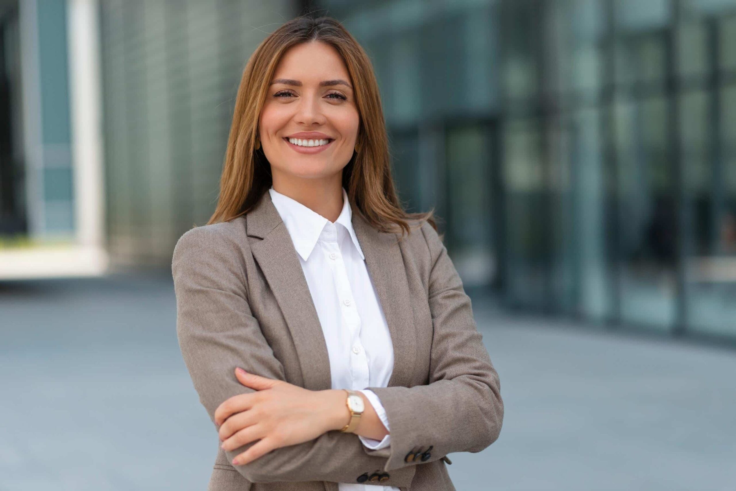 Confident female executive protection agent in a business suit standing outside a corporate building with arms crossed