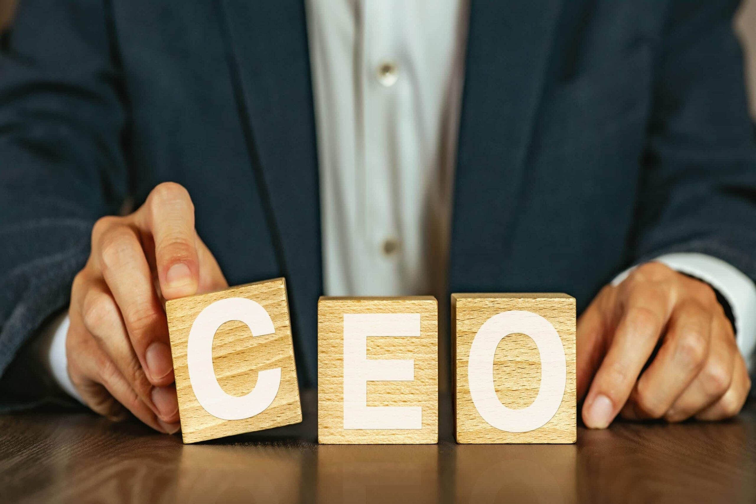Business executive arranging wooden CEO letter blocks representing private security for CEO leadership protection